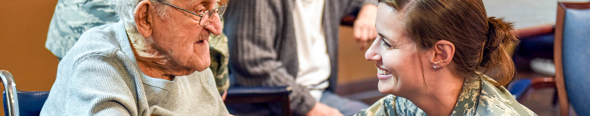A smiling female veteran helping an elderly man in a wheelchair